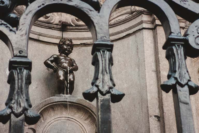 A close-up of the Manneken Pis statue in Brussels, seen through an ornate iron fence.
