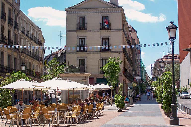 Uma animada cena de rua em Madri com assentos ao ar livre e um edifício histórico.