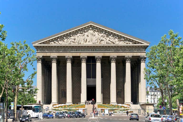 La Madeleine Church with massive Corinthian columns and classical temple facade framed by green trees against blue sky