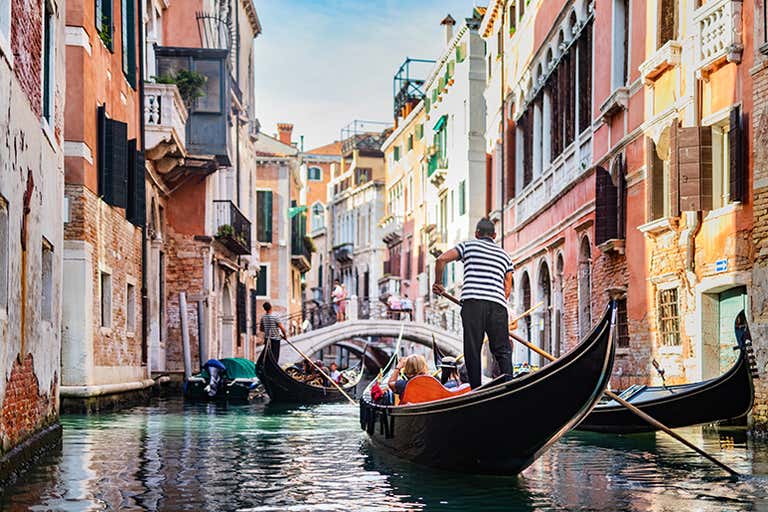 Traditionelle Gondelfahrt durch den engen venezianischen Kanal mit bunten Gebäuden und einer kleinen Brücke, ein typisches Venedig-Erlebnis