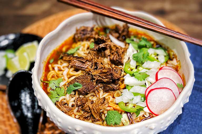 Spicy ramen topped with shredded beef, radishes, cilantro and jalapeños, served with lime wedges and chopsticks.