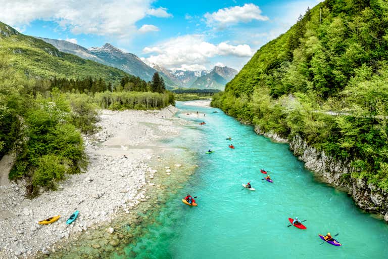 Turquoise waters of Soča River wind through Julian Alps, with kayakers paddling the crystal-clear stream surrounded by lush mountains