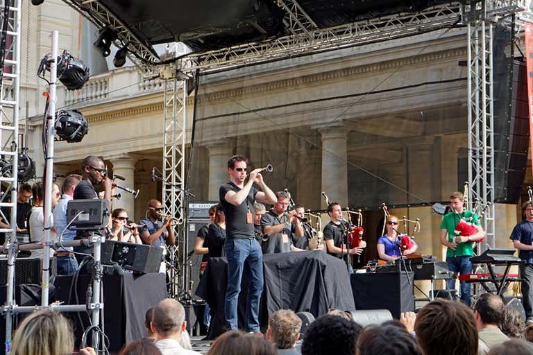 Músicos se apresentam ao vivo no palco da Fête de la Musique em Paris, com uma multidão reunida em volta aproveitando o evento vibrante.