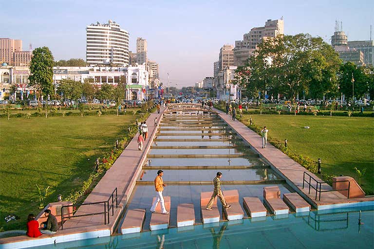 Vista de Connaught Place, em Nova Délhi, com pessoas caminhando em uma área de parque.