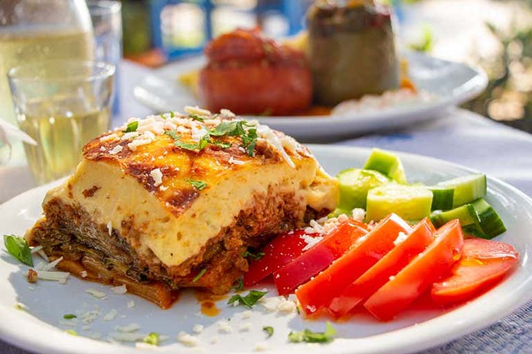 Een bord moussaka met gesneden tomaten en komkommers, buiten geserveerd