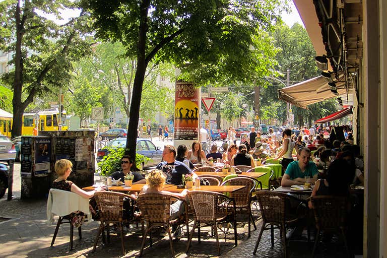 A bustling outdoor café in Berlin with people enjoying breakfast under trees.