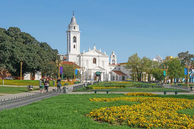 White colonial church with bell tower and landscaped gardens in Buenos Aires neighborhood.