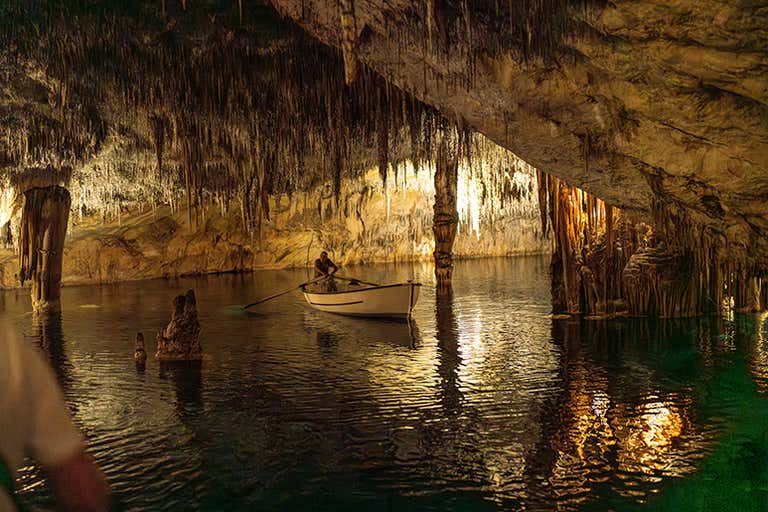 A person rowing a boat inside the illuminated Cuevas del Drach in Mallorca.