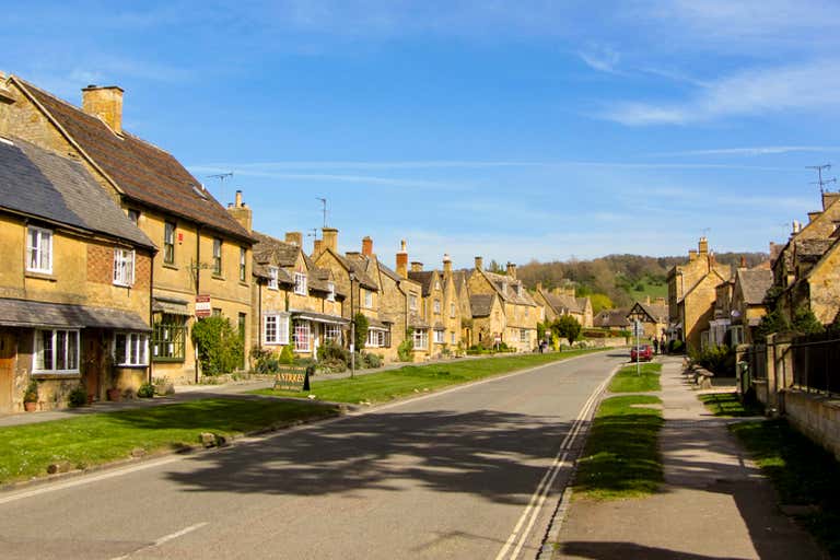 A picturesque street in Chipping Campden, Cotswolds, with traditional stone houses and a clear blue sky.