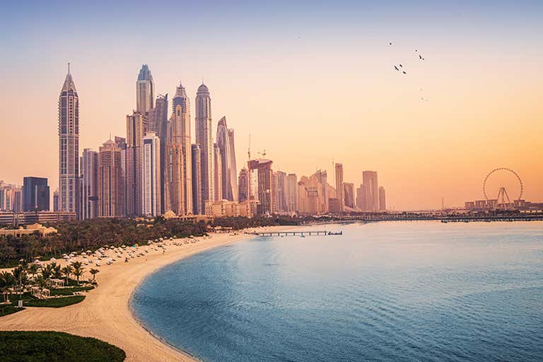 Een prachtige zonsondergang over de skyline van Dubai Marina met een strand op de voorgrond.