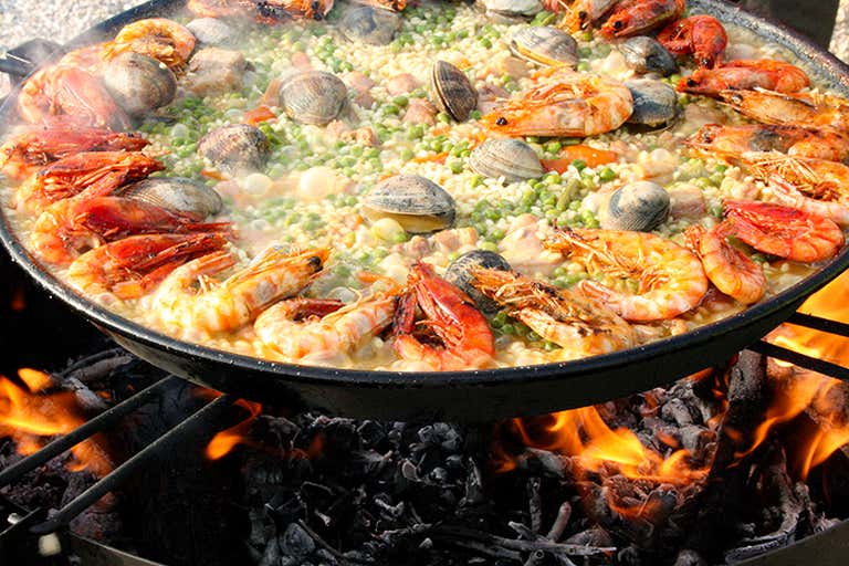 A large pan of seafood paella cooking over an open flame.