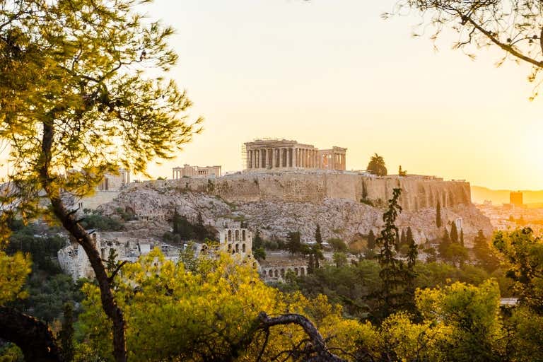 Sunrise over the Acropolis in Athens with trees in the foreground.
