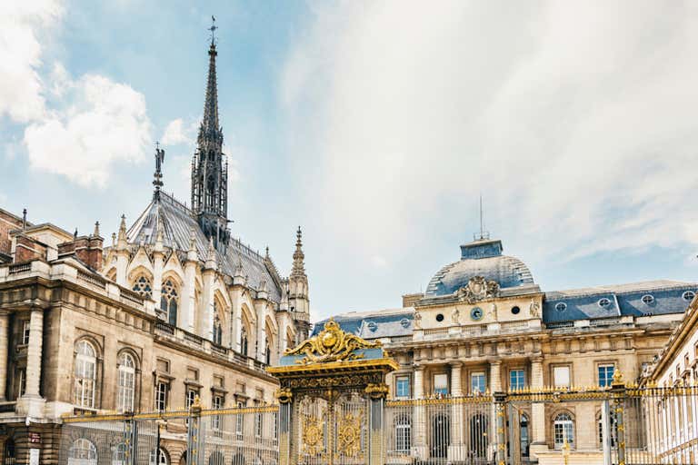 Sainte-Chapelle's ornate Gothic spire and golden gates visible from the Palais de Justice courtyard under blue sky