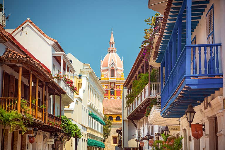 Colorful colonial buildings line a street in Cartagena with the Cathedral of Cartagena in the background.