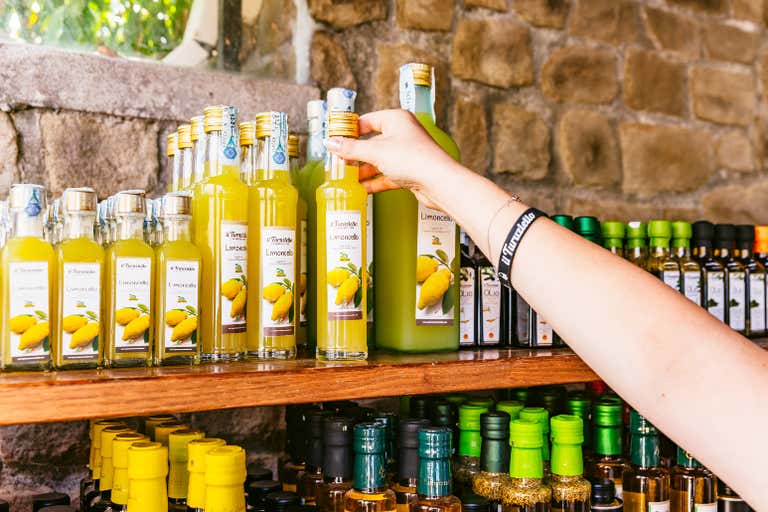 Eine Hand greift nach einer Flasche Limoncello auf einem Holzregal, das mit verschiedenen Flaschen gefüllt ist.