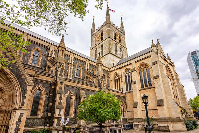 Southwark Cathedral exterior with contrasting stone colors, Gothic windows, central tower and green tree in foreground