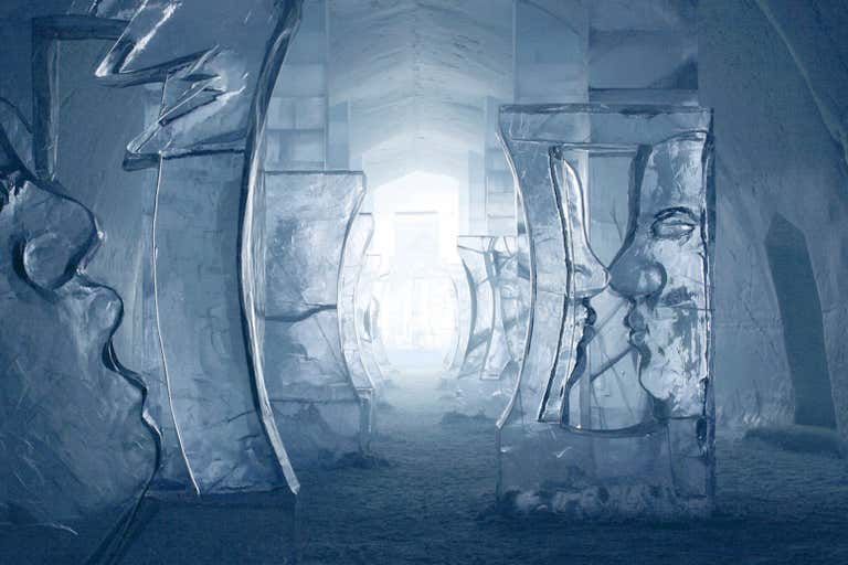 Corredor interno do ICEHOTEL com paredes de gelo esculpidas que brilham em azul e esculturas artísticas de gelo.