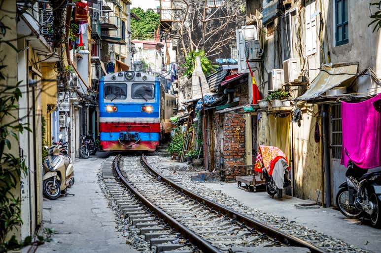 Train passing through a narrow residential street on the Reunification Express in Hanoi, Vietnam.