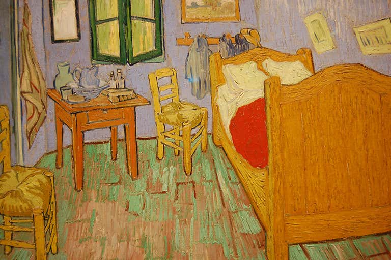 El cuadro "El dormitorio" de Vincent van Gogh muestra una habitación sencilla con cama de madera, sillas, mesa, y unas características paredes azules y suelo verde.