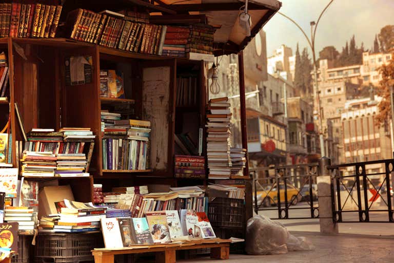 A street bookstall in Amman, Jordan, with historic buildings in the background.