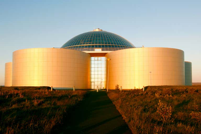 Un edificio moderno con cúpula de cristal y estructuras cilíndricas, bañado por la luz dorada del sol.