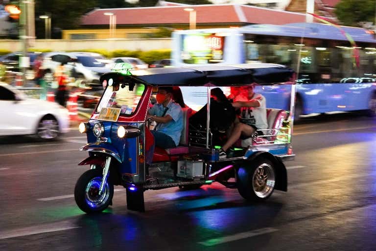 Um tuk-tuk colorido navegando em uma rua movimentada à noite.