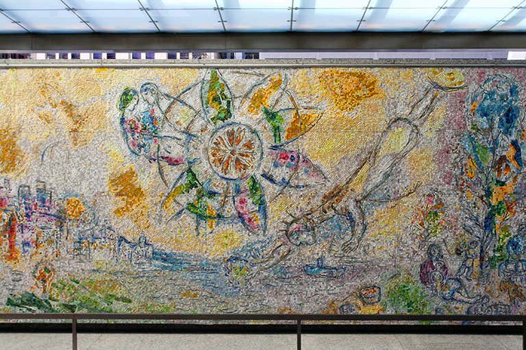 Un colorido mural de mosaico con figuras abstractas, fondo amarillo y motivos circulares, probablemente de Marc Chagall, expuesto en un espacio público de Chicago.