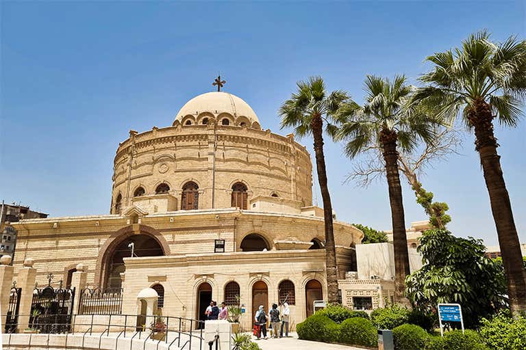 Saint George Church in Cairo with a domed roof, arched windows, palm trees, and visitors exploring the historic site.