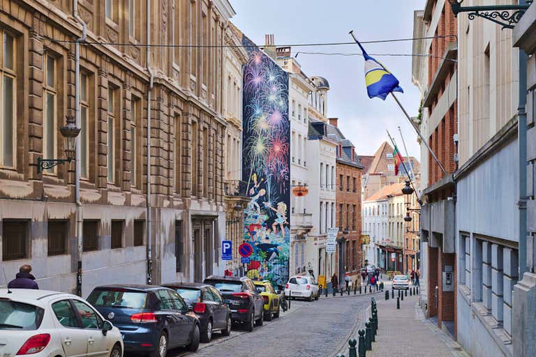 A narrow street in Brussels with a colorful mural depicting fireworks on a building wall.