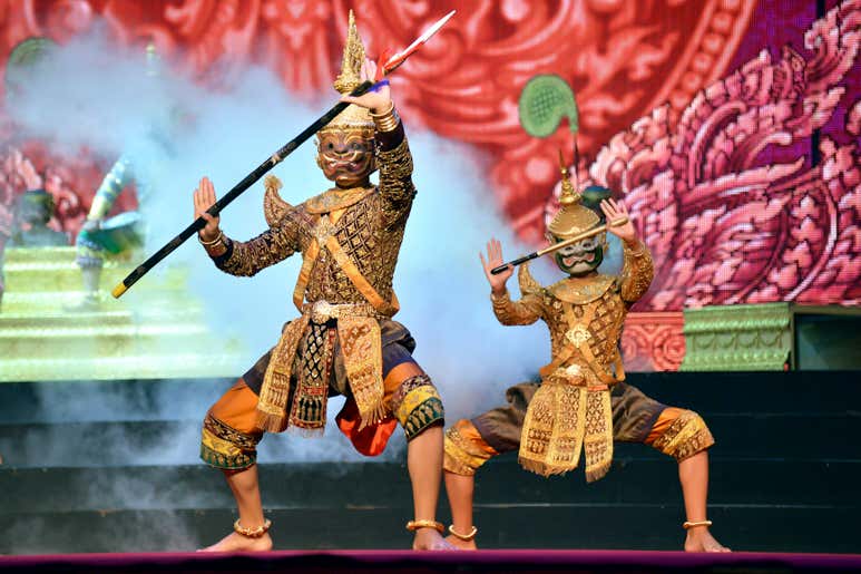 Два исполнителя в традиционных тайских костюмах танцуют на сцене шоу «Сиам Нирамит», а на заднем плане поднимается дым.