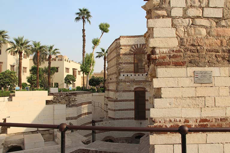Ancient brick and stone ruins surrounded by palm trees under a clear blue sky in Cairo.