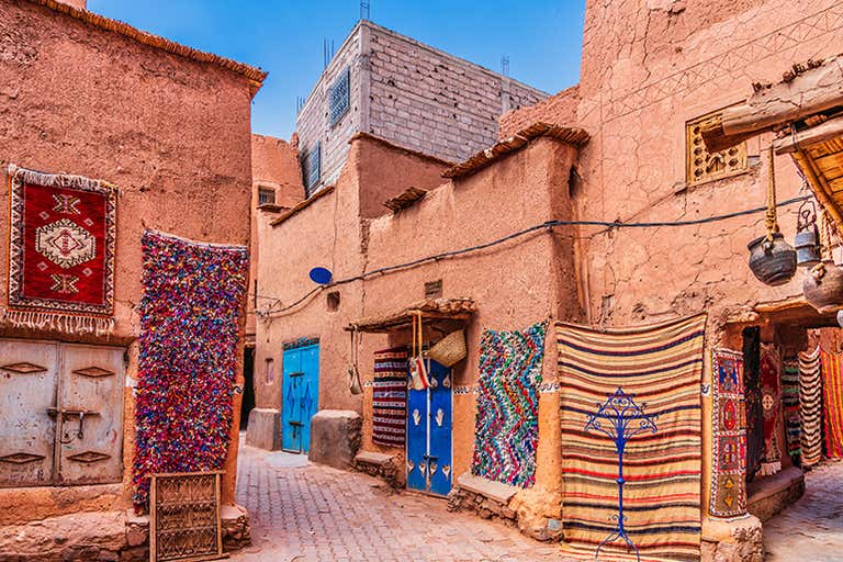 Una vibrante calle de la Medina de Marrakech con coloridas alfombras colgadas de las paredes.