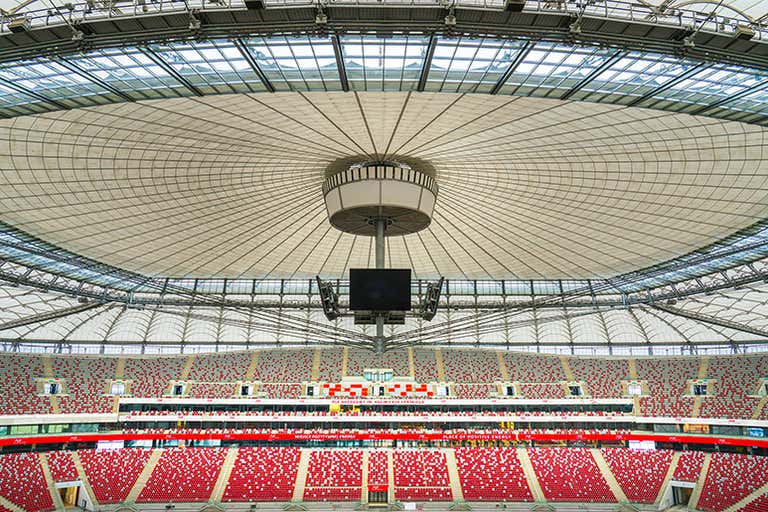 Uma foto em grande angular do interior do Estádio Nacional, com seu grande teto circular e fileiras de assentos vermelhos e brancos.