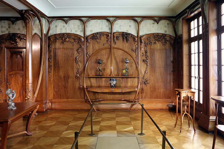 Elegant Art Nouveau room with intricate wood paneling, decorative shelves, and parquet flooring.