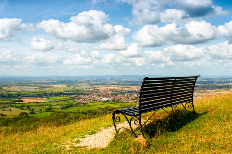 A scenic view from Cleeve Hill with a bench overlooking the countryside.