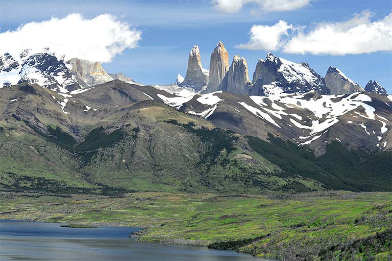 Uma vista panorâmica de Torres del Paine com picos cobertos de neve e um lago.