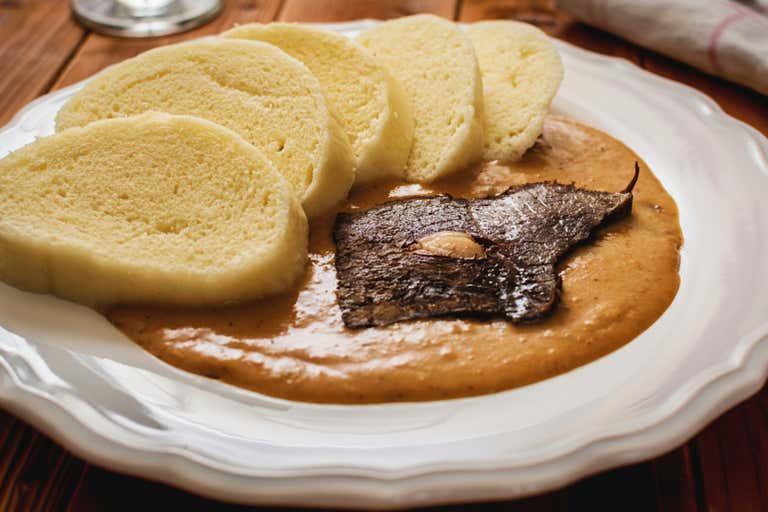 Um prato de svíčková tcheco com bolinhos e molho cremoso.