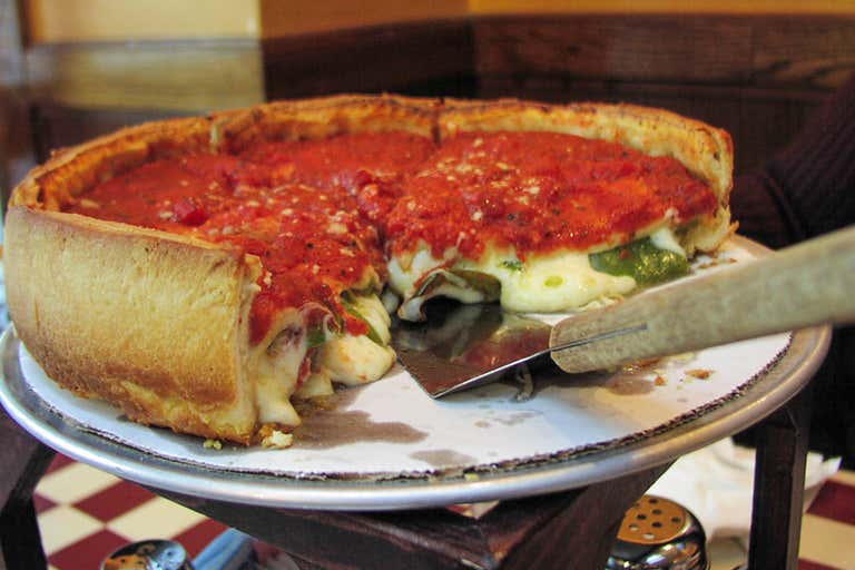 Una pizza estilo deep-dish con una porción servida en una bandeja metálica.