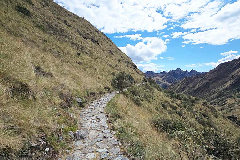 Um caminho de pedra que serpenteia por uma paisagem montanhosa sob um céu azul com nuvens.