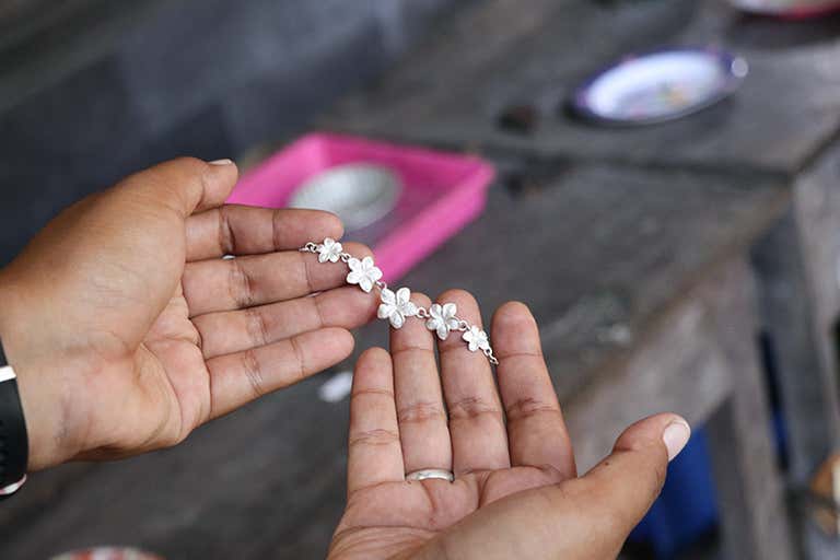 Manos sosteniendo una delicada pulsera floral en un taller.