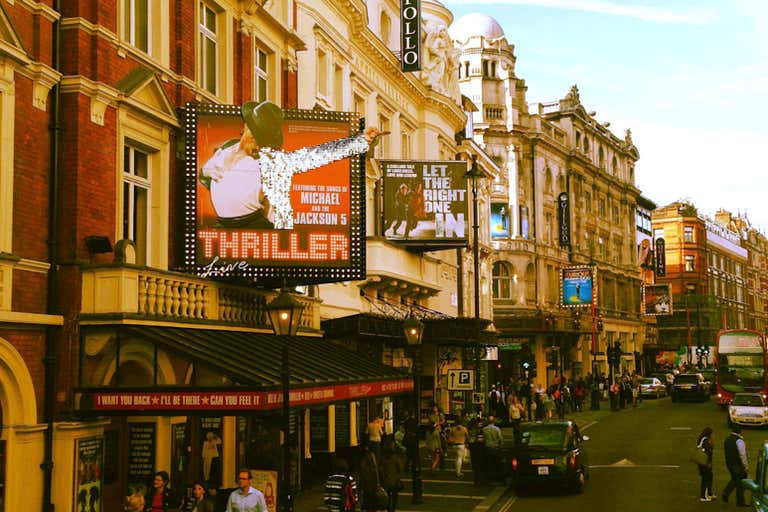 A busy street in London's West End with theater signs and people walking.