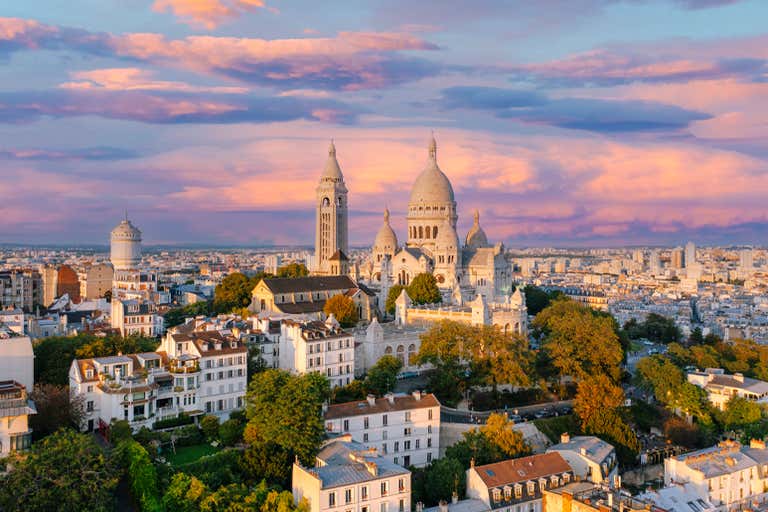 Sacre-Coeur Basilica's white domes glowing at sunset atop Montmartre hill with panoramic view of Paris rooftops below