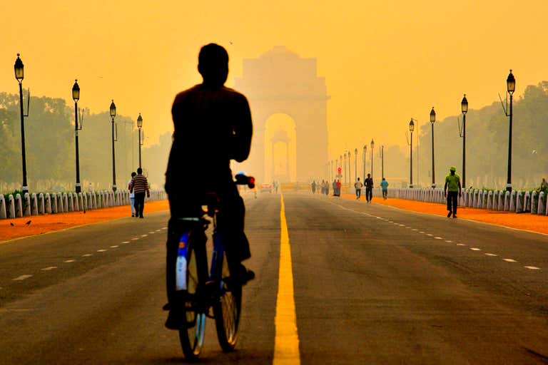 Um ciclista pedala em direção ao India Gate em Nova Déli durante o pôr do sol.