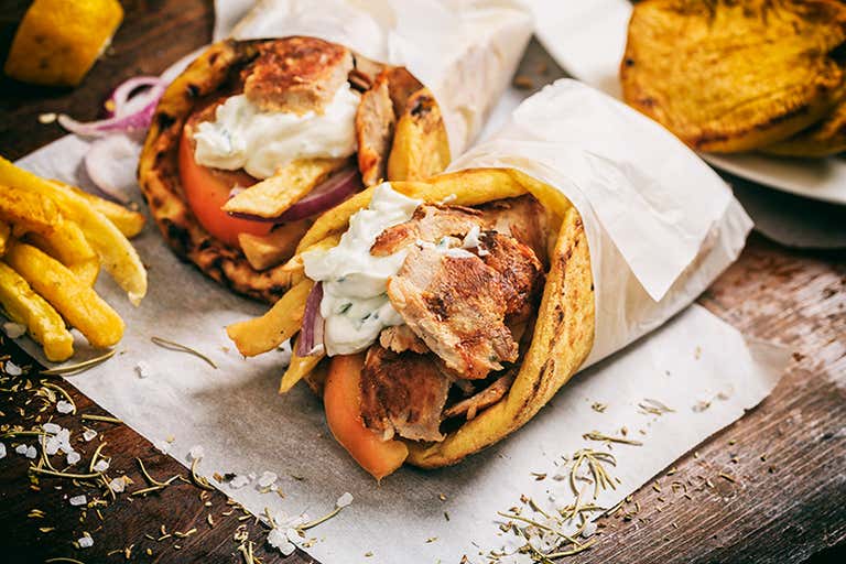 Two gyros wraps with fries and tzatziki sauce on a wooden table