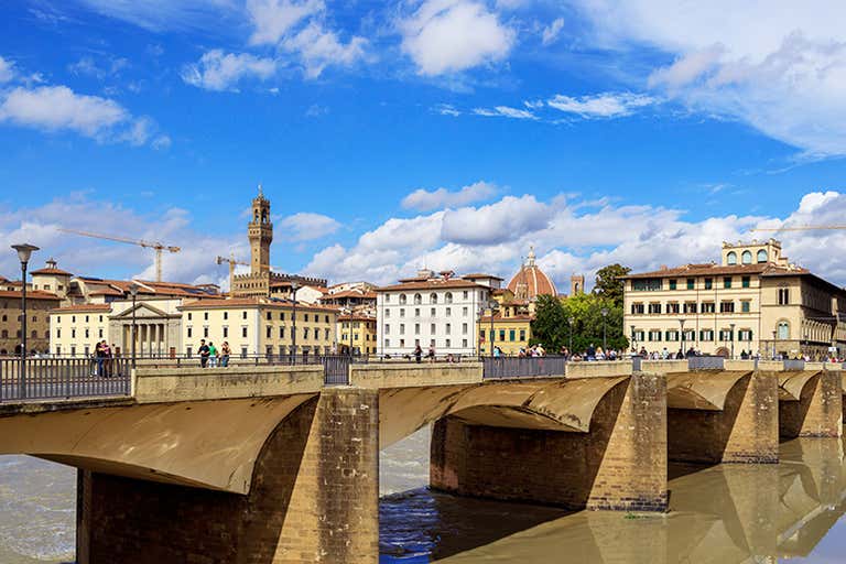 Een stenen brug in Florence met historische gebouwen en een blauwe lucht.