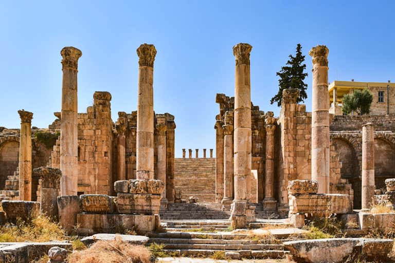 Ancient Roman ruins with tall columns and stone staircases at Jerash under clear blue sky.