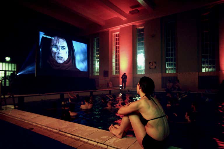 Personas viendo una película mientras están sentadas en una piscina.