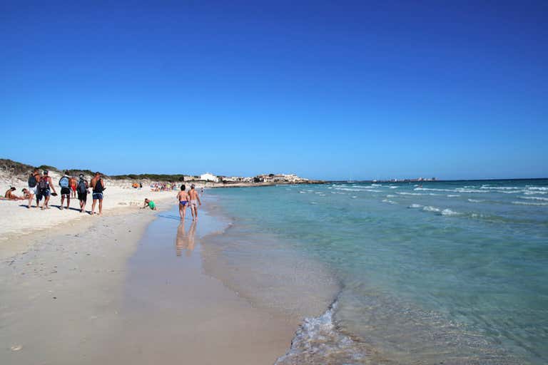 A sunny beach with people walking along the shore in Mallorca.