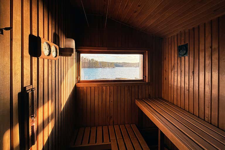 Interior da sauna tradicional de madeira com janela com vista para o lago, bancos e termômetro.