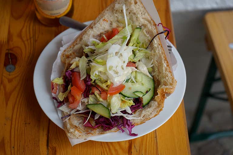 A döner kebab filled with fresh vegetables on a white plate
